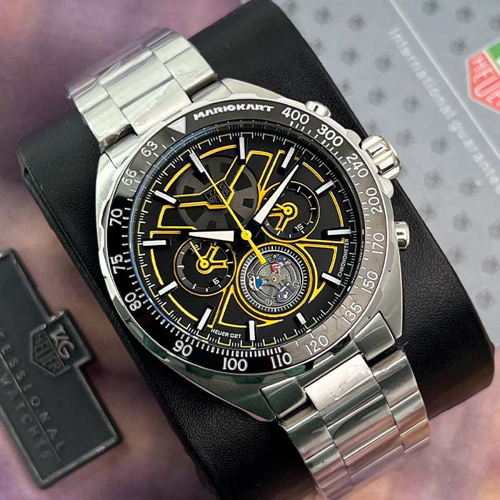 Reloj estilo TAG Heuer Mario Kart con detalles en amarillo, esfera negra y pulso metálico brillante para look deportivo sofisticado.