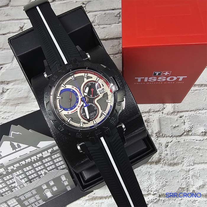 Reloj Tissot T-Race edición especial con diseño automovilístico, carátula plateada, detalles en rojo y azul, y correa negra tipo rally.