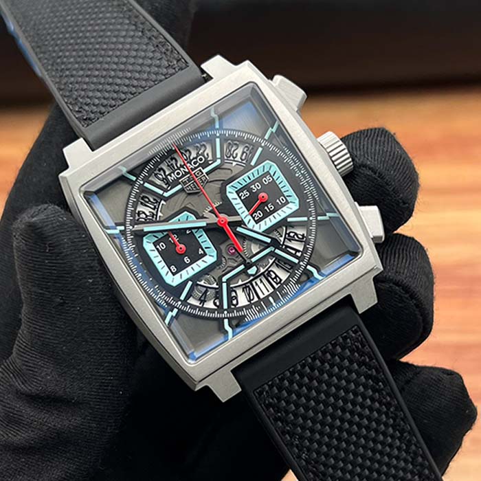 Reloj TAG Heuer Monaco estilo deportivo con caja cuadrada, carátula esqueletada y detalles en azul hielo sobre correa negra.