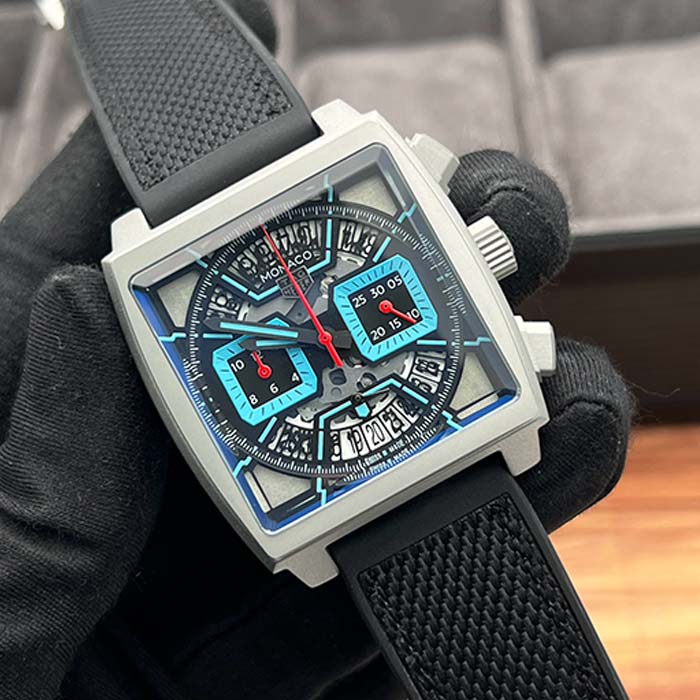 Reloj TAG Heuer Monaco con caja cuadrada, detalles en azul hielo, correa negra deportiva y diseño tipo skeleton.