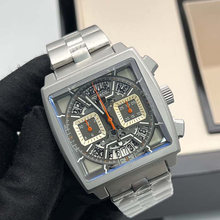 Reloj TAG Heuer Monaco skeleton plateado con caja cuadrada, correa metálica y marcadores naranjas deportivos.