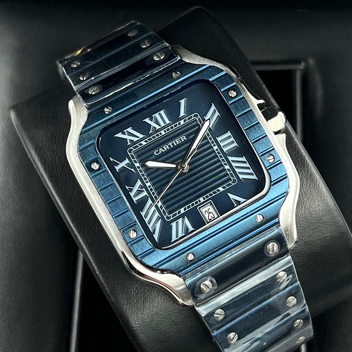 Reloj Cartier Santos azul metálico para hombre con caja cuadrada, números romanos, y correa de acero pulido, ideal para un estilo moderno y elegante.