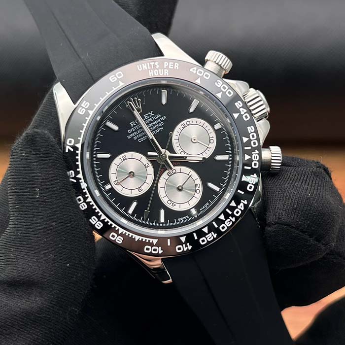 Reloj tipo Rolex Daytona con esfera negra, subesferas plateadas y correa de caucho negra, estilo deportivo de lujo.