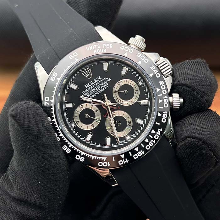 Reloj estilo Rolex Daytona con correa de caucho, esfera negra y detalles dorados en subesferas.